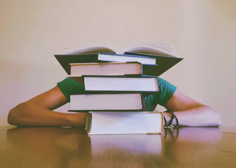 Person studying with a stack of books in the foreground.