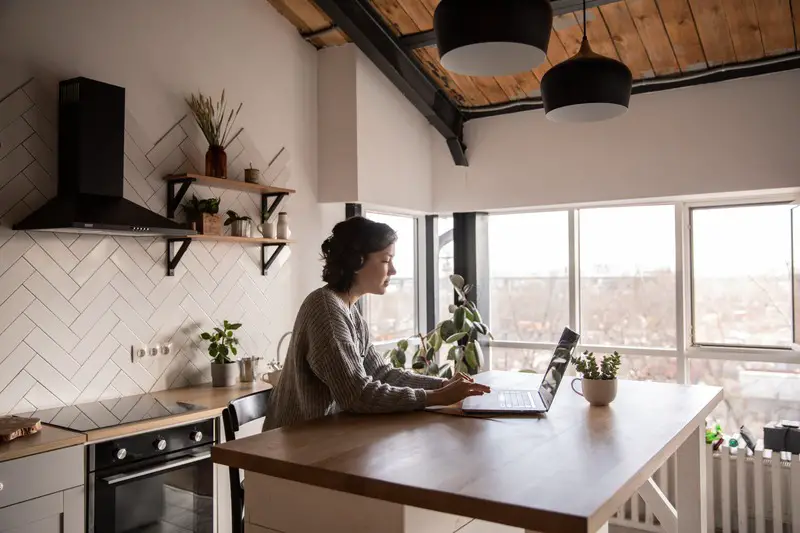 Woman multitasking in the kitchen with a laptop.